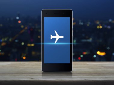Ahşap masa üzerinde modern akıllı telefonun ekranında uçak simgesini bulanıklık renkli gece ışık şehir Kulesi, iş ulaşım kavramı