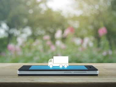 Kamyon düz ahşap masa üzerinde modern akıllı telefonun ekranında simgesine bulanıklık Pembe çiçek ve ağaç, iş ulaşım hizmeti kavramı