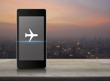 Ahşap masa üzerinde modern akıllı telefonun ekranında uçak simgesini bulanıklık cityscape sıcak ışık sundown, iş ulaşım kavramı