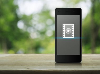 Oynat düğmesini ahşap masa üzerinde modern akıllı cep telefonu ekranda film simgesi ile bulanıklık yeşil ağaç Park, iş sinema online kavramı