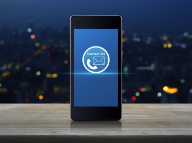 Telefon ve e-posta kutsal kişilerin resmi düğme ahşap masa üzerinde modern akıllı cep telefonu ekranda görüntü renkli gece ışık şehir kule ve gökdelen, iş kavramı bize ulaşın