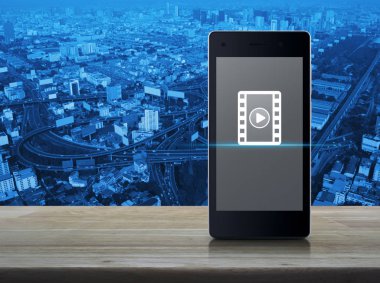Film simgesi ile ahşap masa üzerinde modern akıllı cep telefonu ekranındaki Yürüt düğmesi Şehir Kulesi, sokak, otoyol ve gökdelen, sinema online kavramı üzerinde