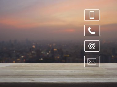 Telefon, mobil telefon, adres ve e-posta düğmeleri ahşap masa üzerinde bulanıklık modern şehir bina kule ve gökdelen üzerinde sıcak ışık gün batımından, iş müşteri destek ve hizmet kavramı