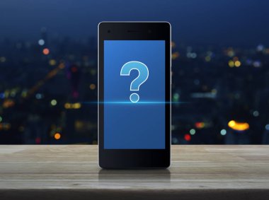 Ahşap masa üzerinde modern akıllı cep telefonu ekran üzerinde soru işaretinin görüntülenmesi bulanıklık renkli gece ışık şehir kule ve gökdelen, iş müşteri destek online kavramı