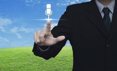 Mavi gökyüzü, iletişim iş kavramı ile yeşil çim alanın üzerinde mikrofon düz simgesine basarak işadamı