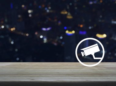 CCTV kamera simgesi üzerinde ahşap masa üzerinde bulanıklık renkli gece ışık şehir kule ve gökdelen, iş güvenlik online kavramı