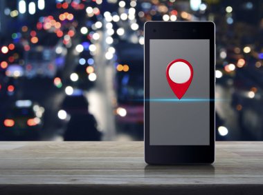 Ahşap masa üzerinde üzerinde modern akıllı cep telefonu ekranındaki harita PIN konumu düğmesini bulanıklık arabalar ve road, harita işaretçi gezinti kavramı ile şehrin renkli gece lambası