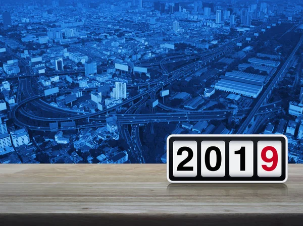 Retro flip clock with 2019 text on wooden table over modern office city tower, street, expressway, and skyscraper, Happy new year concept