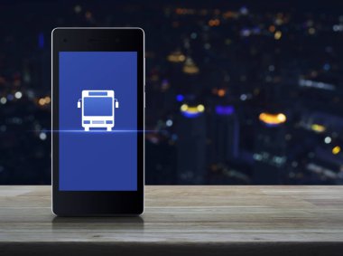 Otobüs düz ahşap masa üzerinde modern akıllı cep telefonu ekran simgesine bulanıklık renkli gece ışık şehir kule ve gökdelen, iş ulaşım hizmeti çevrimiçi kavramı