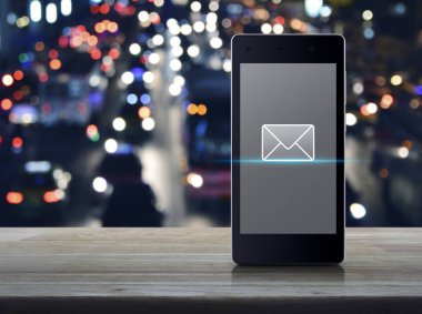 ahşap masa üzerinde modern akıllı cep telefonun ekranında e-posta simgesini bulanıklık araçları, online iletişim iş kavramı ile renkli gece ışık şehir