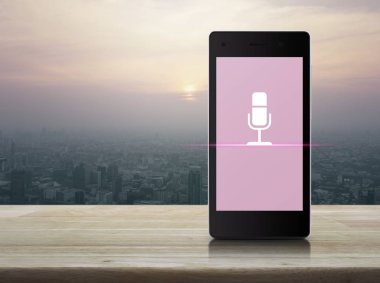Modern akıllı cep telefonu ekranındaki mikrofon düz simgesi ahşap masa üzerinde ve günbatımında gökdelen, klasik tarz, iş iletişimi çevrimiçi konsepti