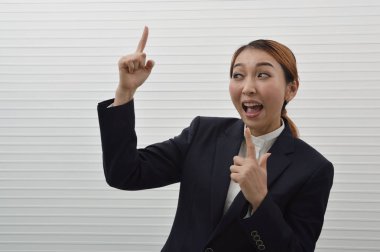 Mutlu Genç Asyalı işkadını siyah takım elbise ve beyaz duvar arka plan üzerinde duran, yüz ifadesi gülümseyen beyaz gömlek portresi