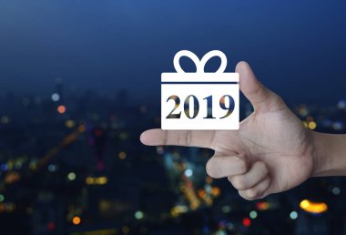 Hediye kutusu mutlu yeni yıl 2019 düz kutsal kişilerin resmi üstünde parmak üzerinde bulanıklık renkli gece ışık şehir kule ve gökdelen, iş kavramı alışveriş
