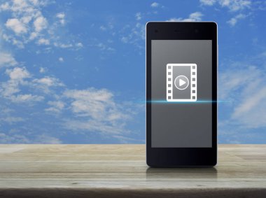 Düğme film simgesi ile modern akıllı cep telefonu ekran üzerinde ahşap masa mavi gökyüzü beyaz bulutlar, iş sinema online kavramı ile oynayın