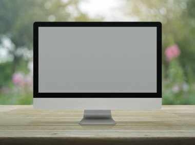 Masaüstü modern bilgisayar monitörü ile bulanıklık pembe çiçek ve ağaç üzerinde ahşap masa üzerinde geniş gri perde