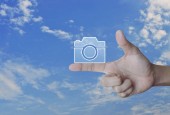 Plochý ikonu fotoaparátu na prst nad modrou oblohu s bílé mraky, obchodní fotoaparát služby obchod koncept