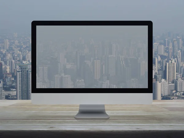 Desktop modern computer monitor with wide screen on wooden table over office building tower and skyscraper in city