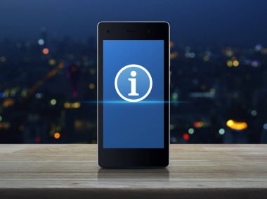Ahşap masa üzerinde modern akıllı cep telefonu ekranda bilgi işareti simgesini bulanıklık renkli gece ışık şehir kule ve gökdelen, online iletişim iş kavramı