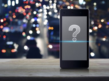 Ahşap masa üzerinde modern akıllı cep telefonu ekran üzerinde soru işaretinin görüntülenmesi bulanıklık otomobil City, iş müşteri destek online kavramı ile renkli gece ışık şehir