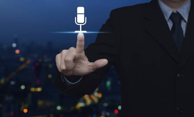Bulanık renkli gece ışık şehir kule ve gökdelen, iletişim iş kavramı üzerinde mikrofon düz simgesine basarak işadamı