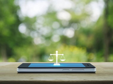 Modern akıllı cep telefonu ekranındaki yassı simge parktaki bulanık yeşil ağacın üzerindeki ahşap masada, iş hukuku hizmetleri online konsepti