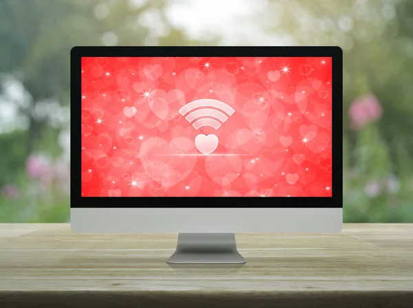Wifi 平面图标桌面现代电脑显示器与红色屏幕上的木桌模糊的花和树在公园 互联网在线爱情连接 情人节概念 — 图库照片