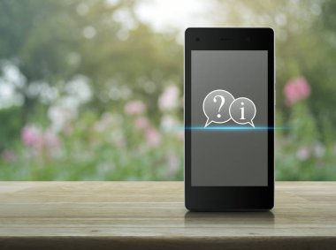 Soru işareti ve ahşap masa üzerinde modern akıllı cep telefonu ekranda bilgi sohbet simgesini pembe çiçek ve Bahçe, iş Müşteri Hizmetleri ağacında bulanıklığı ve online kavramı destek