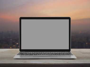 Ahşap masa üzerinde boş gri ekran ile modern dizüstü bilgisayar bulanıklık cityscape sıcak ışık gün batımından üzerinde