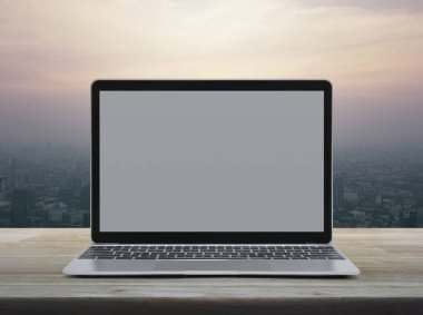 Modern dizüstü bilgisayar üzerinde office şehir kule ve gökdelen günbatımı gökyüzüne, vintage tarzı ahşap masa boş gri ekran ile