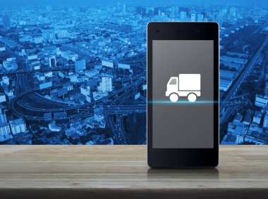 Kamyon teslim düz üstünde kutsal kişilerin resmi Şehir Kulesi, street, otoyol ve gökdelen, iş ulaşım online kavramı üzerinde ahşap masa ekranda modern akıllı cep telefonu