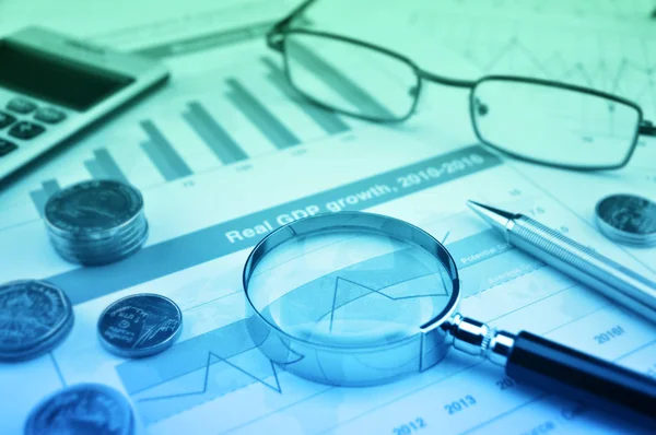 Magnifying glass, pen, coins, calculator and glasses on growth f — Stock Photo, Image