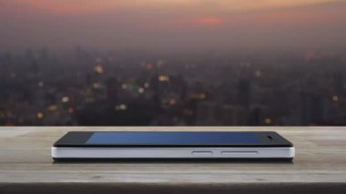 Sıcak ışık günbatımı nda cityscape bulanıklık üzerinde ahşap masada modern akıllı cep telefonu ekranında otobüs düz simgesi, İş taşımacılığı online hizmet konsepti