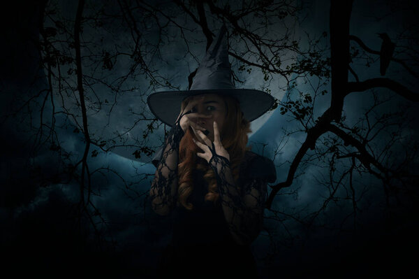Scary halloween witch standing over dead tree, crow, birds, full moon and spooky cloudy sky, Halloween mystery concept