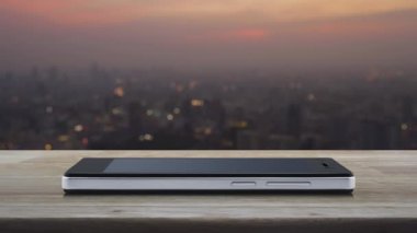 Günbatımında şehir manzarası bulanıklığı üzerine ahşap masadaki modern akıllı cep telefonu ekranına düz simge indir, Teknoloji İnternet konsepti