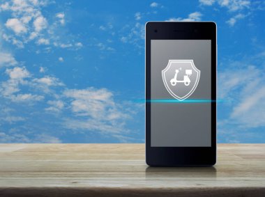 Motosiklet, kalkanın düz simgesi, modern akıllı cep telefonu ekranında, mavi gökyüzü üzerinde, beyaz bulutlu ahşap masa üzerinde, iş motosikleti sigortası, online konsept.