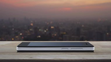Günbatımı, iş güvenliği ve güvenlik online konsepti üzerine şehir manzarası bulanıklığı üzerinde ahşap masa üzerinde modern akıllı cep telefonu ekranı üzerine modüllü CCTV kamera yassı simgesi