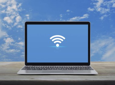 Modern dizüstü bilgisayarı olan Wi-Fi düz ikonu beyaz bulutlu mavi gökyüzü üzerinde ahşap masa üzerinde, teknolojili internet konsepti