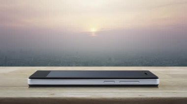 Modern akıllı cep telefonu ekranındaki düğme simgesini şehir kulesinin üzerindeki ahşap masada ve günbatımında gökdelen, klasik tarz, iş müziği çevrimiçi konseptinde oynat