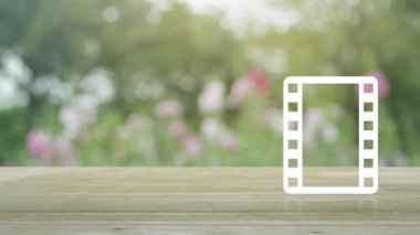 Tahta masadaki film yassı ikonu ile bahçedeki bulanık pembe çiçek ve ağaç üzerinde oynama düğmesi, iş sineması çevrimiçi kavramı