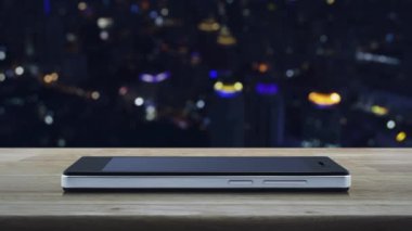 Modern akıllı cep telefonu ekranında düz simge oynat ahşap masa üzerinde bulanık gece lambası şehir kulesi ve gökdelen, iş müziği online konsepti
