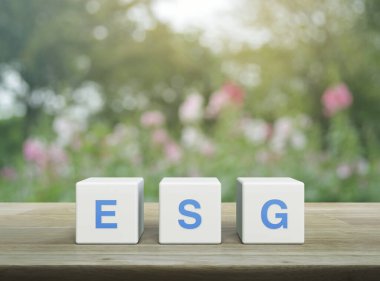 Beyaz blok küplere ESG kısaltması. Tahta masa, bulanık pembe çiçek ve bahçede ağaç. Çevresel Sosyal Yönetim kavramı.