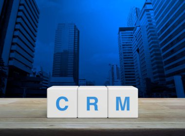 CRM kısaltması beyaz blok küpleri üzerinde ahşap masa üzerinde modern ofis kulesi ve gökdelen üzerinde, Müşteri İlişkileri Yönetimi konsepti