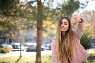 Genç, güzel, sarışın, pembe ceketli, başparmağıyla parkta.  