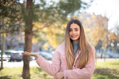 Genç ve güzel bir kadın parkta avuç içi gösteriyor.  