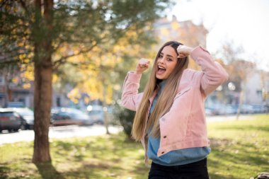 Genç ve güzel sarışın hippi kadın, gündelik giysiler giyip çılgınlığı kutluyor ve başarıya hayret ediyor. Kolları açık, gözleri açık, heyecanla bağırıyor. Kazanan konsept. Dışarıda dikiliyorum.