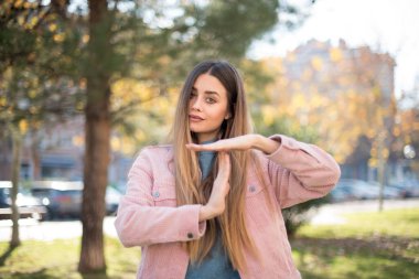 Pembe ceketli güzel sarışın kadın parkta el kol hareketi yapıyor.  