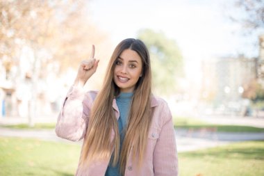 Pembe ceket giyen, ağzı açık, gülümseyen ve neşeli bir ifade takınan genç, çekici sarışın kadın, dışarıda inanılmaz bir şey gösteriyor. Reklam kavramı.