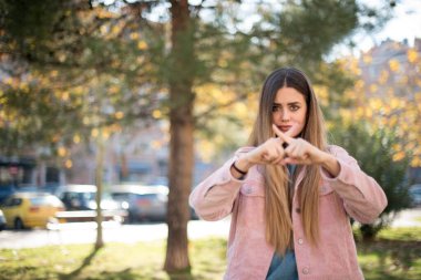 Genç, güzel, sarışın, pembe ceketli, parkta çapraz parmaklı bir kadın.  