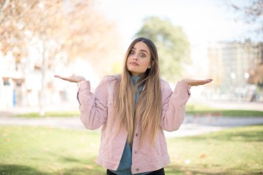 Kafası karışmış, kolları açık pembe ceket giyen, omuzlarını silkeleyen, 