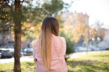 Parkta pembe ceket giyen güzel sarışın bir kadının arka plan görüntüsü.  